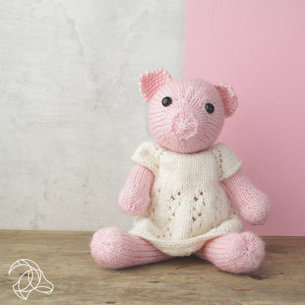 Cute knitted pig in a dress on a wooden surface with a pink and gray background