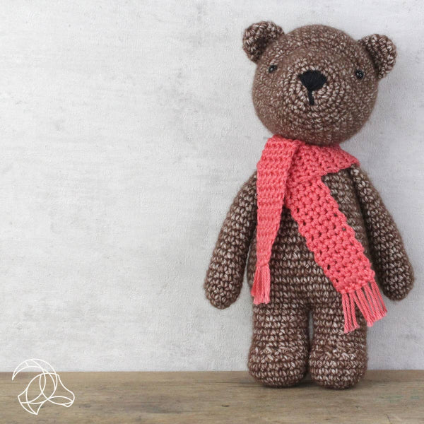 Brown teddy bear with a pink scarf on a wooden surface and light gray background
