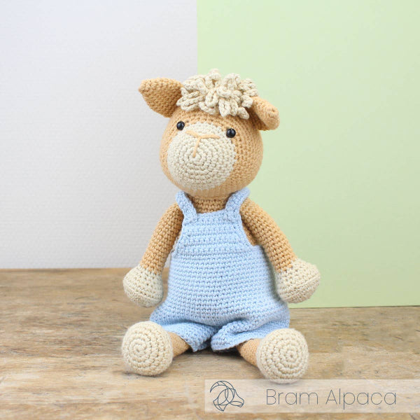 Crocheted alpaca toy wearing a blue romper with a white background