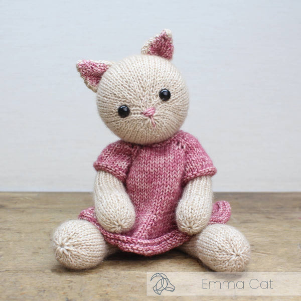 Knitted cat toy with a pink dress on a wooden surface, branded 'Emma Cat'.